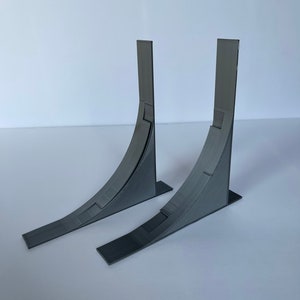 May include: Two gray 3D printed ramps, each with a curved surface and a flat base. The ramps are angled upwards and are positioned side by side.