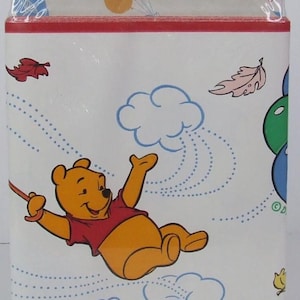 May include: A Winnie the Pooh decorative wall border in original packaging. The package features a yellow bear character, blue clouds, and colorful leaves. Text includes 8.4 sq. ft. (5 yd. x 6.83 in.), PREPASTED, STRIPPABLE, WASHABLE, and BORDEN HOME WALLCOVERINGS.
