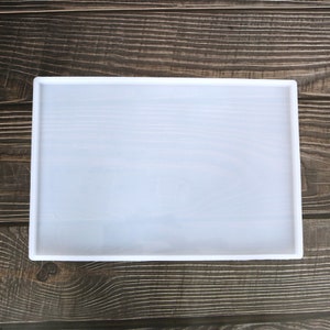 May include: A white silicone mould for resin casting, with a rectangular shape. The mould is on a wooden surface.