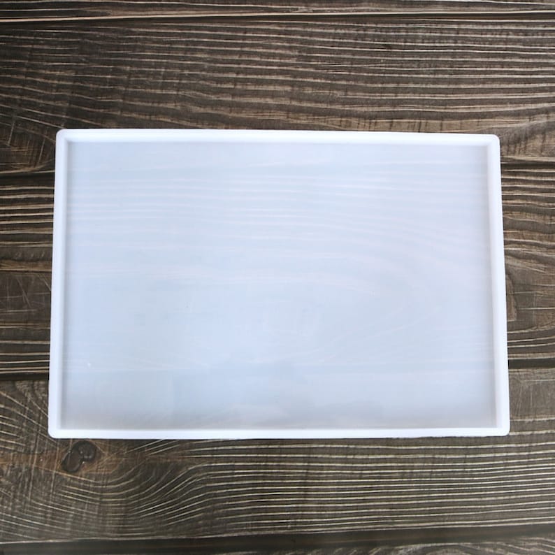 May include: A white silicone mould for resin casting, with a rectangular shape. The mould is on a wooden surface.