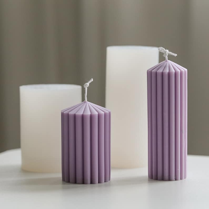 May include: Three candles, two white and one purple, with a ribbed design. The purple candle is the smallest and the white candles are taller.