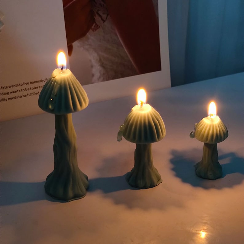 K&ouml;nnte beinhalten: Drei tealblaue kerzen in Pilzform mit einer Flamme, die auf jeder Kerze brennt. Die Kerzen stehen auf einer wei&szlig;en Oberfl&auml;che.