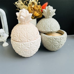 May include: Two pineapple-shaped concrete candle holders. One is gray and the other is pink. Both have a geometric pattern on the surface.
