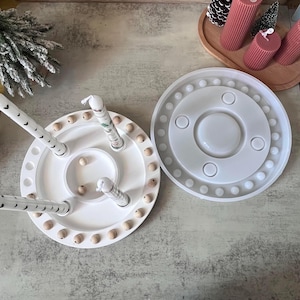 May include: A white, round, wooden candle holder with four legs and a matching mold. The candle holder has wooden beads around the edge and decorative candles. The mold has a series of circles and small spheres.