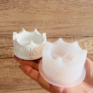 Op de afbeelding: Een witte siliconen mal in de vorm van een kroon met een gedetailleerd ontwerp. De mal ligt op een wit oppervlak.