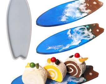 May include: Three miniature cakes on a blue and brown surfboard-shaped resin tray. The tray has a white wave design and brown accents. The cakes are a yellow sponge cake with red and black decorations, a chocolate sponge cake with white frosting and a white sponge cake with green decorations.