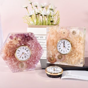 May include: Three decorative clocks with dried flowers encased in clear resin. The clocks are in different shapes, including a hexagon, a square, and a round clock. The clocks have gold-colored hands and Roman numeral markings.