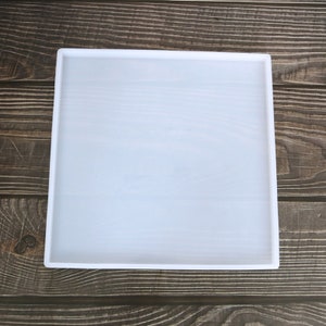 May include: A white silicone square mould for resin casting. The mould is on a wooden surface.