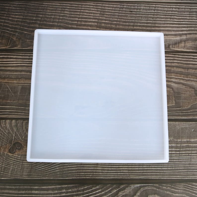 May include: A white silicone square mould for resin casting. The mould is on a wooden surface.