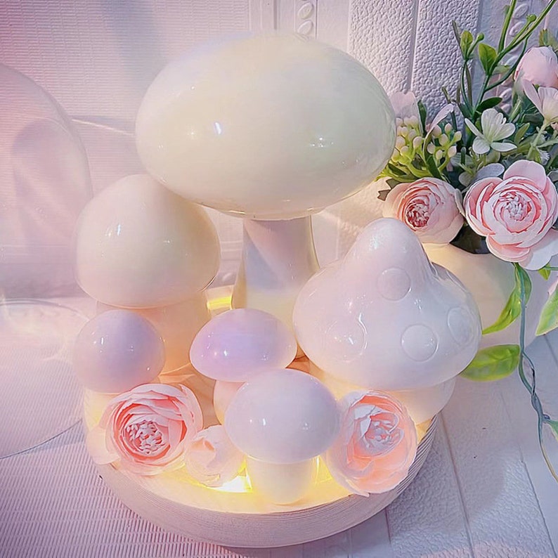 May include: A set of five white ceramic mushroom lamps with a warm white glow. The lamps are arranged on a wooden base with pink flowers.