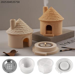 Op de afbeelding: Twee beige keramische kaarsenhouders in de vorm van een huis met rieten daken en schoorstenen. Eén heeft een brandende kaars binnenin. Extra componenten zijn een metalen zeef en witte plastic mallen. Een blad en lucifers zijn ook aanwezig.