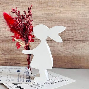 Könnte beinhalten: Ein weißer Holzschnitt eines Hasen, der einen Strauß getrockneter roter Blumen hält. Der Hase steht auf einer weißen Karte mit dem Text "have a grand time".