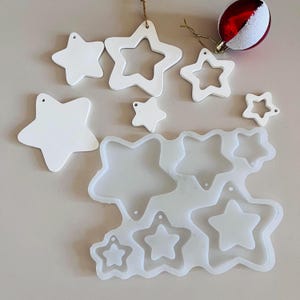 May include: A set of white star-shaped ornaments and a silicone mold with multiple star shapes. The ornaments have holes for hanging. The mold is designed for making resin crafts.