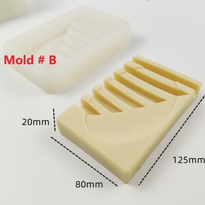 Op de afbeelding: Een beige siliconen mal voor het maken van zeep of hars ambachten. De mal is gevormd als een halve maan met vijf ribben. De mal is 80 mm breed, 125 mm lang en 20 mm diep. De tekst "Mold # B" is op de mal gedrukt.