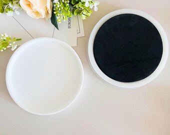 May include: Two round white coasters, one with a black center. The coasters are on a white surface.
