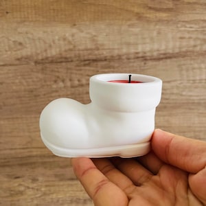 May include: White ceramic candle holder shaped like a Santa boot with a red candle inside.