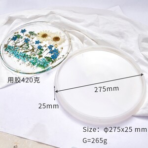 May include: A white silicone mold for resin casting, measuring 275 mm in diameter and 25 mm in height. The mold is shown next to a finished resin tray with pressed flowers, measuring 420 grams. The finished tray is clear with blue and white flowers.