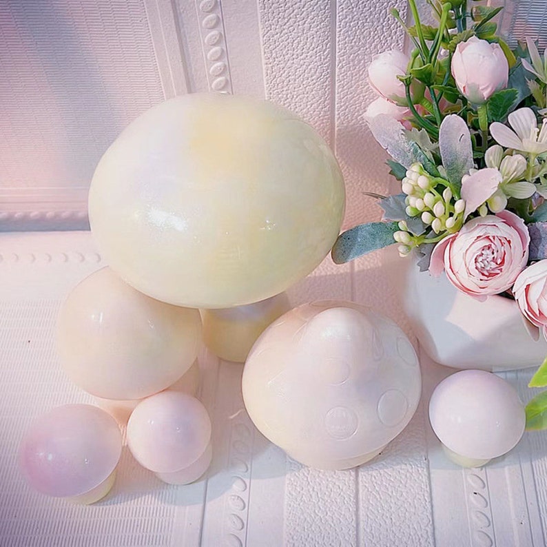 May include: A set of six white ceramic mushrooms of varying sizes. The largest mushroom has a light yellow hue and a glossy finish. The mushrooms are arranged on a white surface.