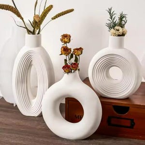 Pode incluir: Três vasos de cerâmica branca com diferentes desenhos geométricos. Os vasos estão vazios e têm um acabamento fosco. Os vasos estão dispostos sobre uma superfície de madeira.