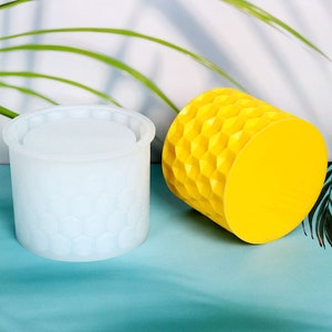 May include: Two silicone moulds for making candles or soap. The moulds are shaped like a cylinder with a honeycomb pattern. One mould is white and the other is yellow.