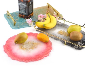 May include: Three resin serving trays with gold leaf accents and gold metal handles. The trays are in different shapes and colors: blue, gray, and pink.