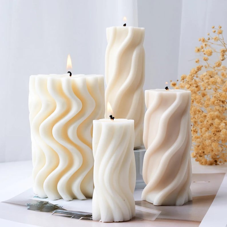 May include: Four white and cream colored candles with a wavy design. The candles are arranged in a row on a white surface.