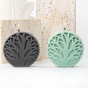 May include: Two round candles with a tree design. The candle on the left is gray and the candle on the right is green.