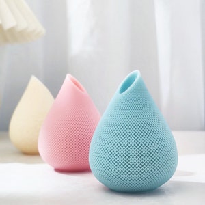 May include: Three ceramic vases shaped like teardrops. The vases are light blue, pink, and cream. The vases have a textured surface.