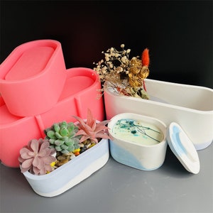 May include: A set of four oval-shaped silicone molds for making concrete planters. The molds are pink and are stacked on top of each other. There are three finished concrete planters, one with a succulent plant, one with dried flowers, and one with a lid.