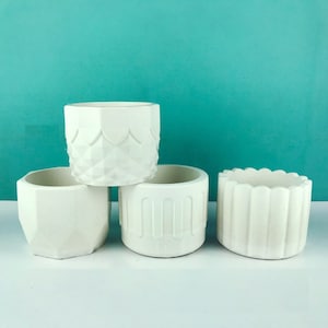 May include: Four white ceramic planters with different geometric designs. The planters are arranged in a pyramid shape, with the largest planter at the bottom and the smallest planter at the top.