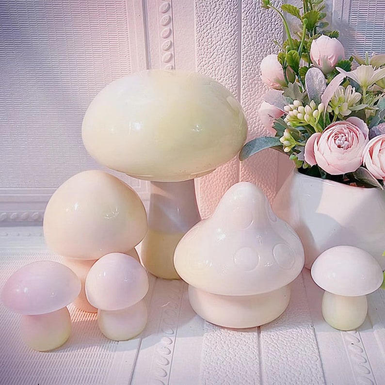 May include: Five ceramic mushroom figurines in various sizes and shades of white and cream. The largest mushroom is a pale yellow color and has a smooth, rounded top. The other four mushrooms are white and have a more textured surface.