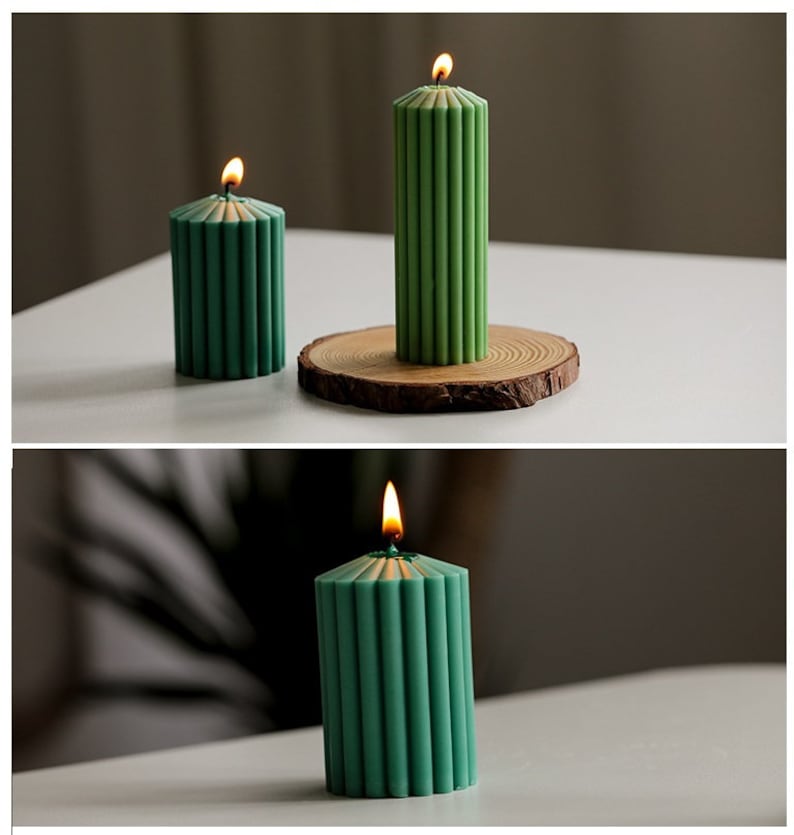 May include: Three green pillar candles with a ribbed design. The candles are lit and have a warm glow. The candles are on a white surface.