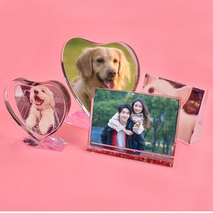 May include: Three heart-shaped crystal photo frames with different images inside. The frames are clear and have a glittery base. The images are of a dog, a couple, and a cat.