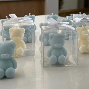 May include: A set of small teddy bear candles in clear plastic boxes with white ribbon bows. The candles are in blue and white.