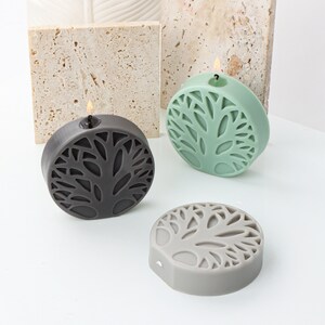 May include: Three round candles with a tree design. The candles are in black, gray, and green.