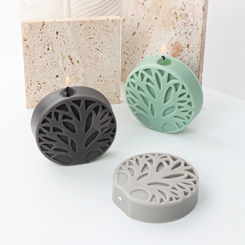 May include: Three round candles with a tree design. The candles are in black, gray, and green.