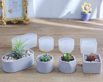 May include: Six different silicone molds for making concrete planters. The molds are in various shapes, including round, oval, and hexagonal. The molds are white and translucent. There are also three small concrete planters with succulents planted in them.