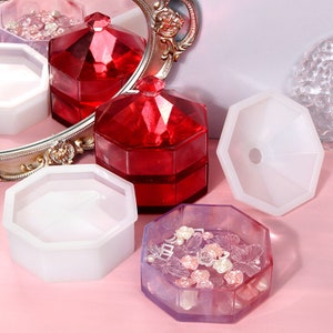 May include: Four octagonal resin moulds for making jewellery boxes. The moulds are white and clear. Two of the moulds are empty and two are filled with resin and decorative elements, including butterflies and flowers.