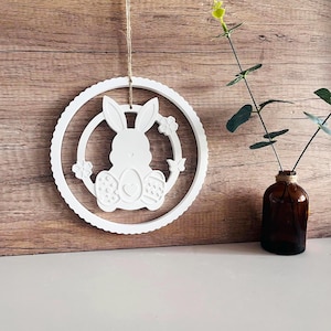 May include: White wooden Easter bunny wreath with a circle design and floral accents. The bunny is holding a heart-shaped egg.