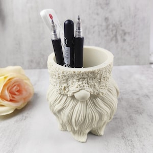 May include: White ceramic gnome pencil holder with a white fuzzy hat and a long white beard. Three black pens are inside the holder.