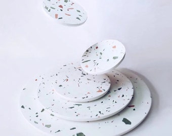 Op de afbeelding: Set van vijf ronde witte onderzetters met een gespikkeld terrazzo-patroon in tinten groen, roze en zwart.