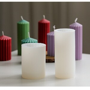 May include: Five candle molds, two are white and three are colored. The colored molds are red, green, and purple. The molds are cylindrical and have a ribbed texture.