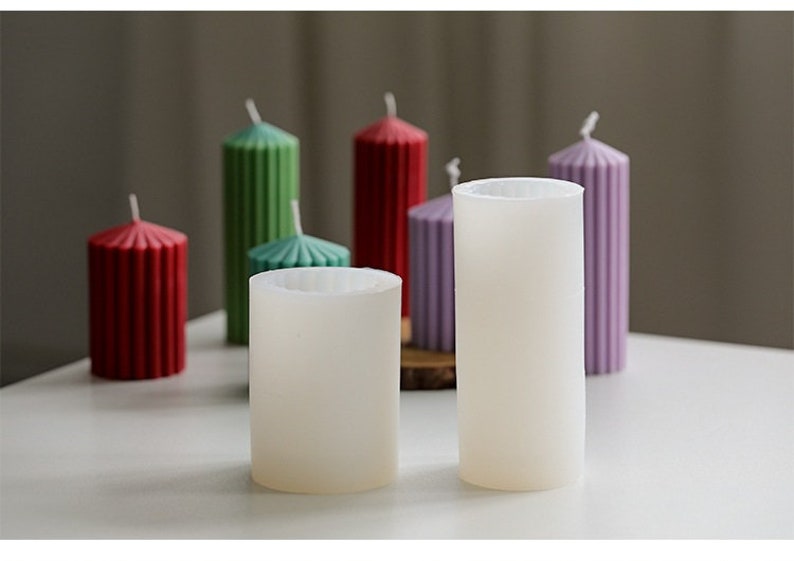 May include: Five candle molds, two are white and three are colored. The colored molds are red, green, and purple. The molds are cylindrical and have a ribbed texture.