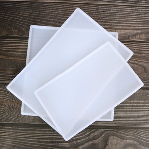 May include: Three white silicone moulds of different sizes, stacked on top of each other. The moulds are rectangular and have smooth edges.