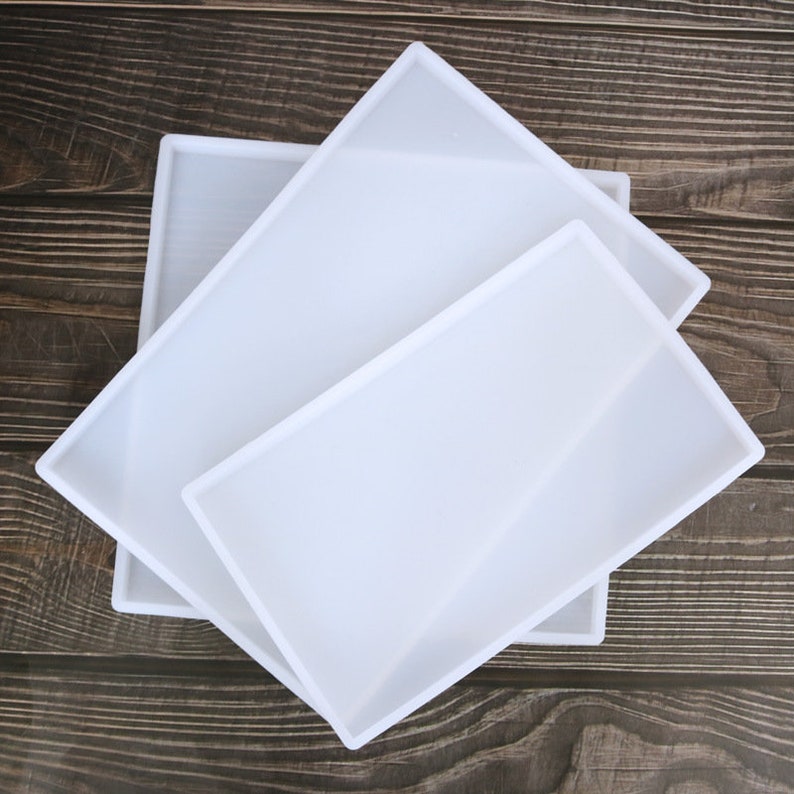 May include: Three white silicone moulds of different sizes, stacked on top of each other. The moulds are rectangular and have smooth edges.