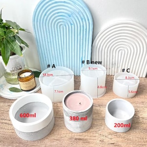 May include: Three silicone molds for making concrete candle holders. The molds are labeled #A, #Bnew, and #C. The molds are different sizes, with the largest mold measuring 12.3 cm in diameter and 7.1 cm in height. The smallest mold measures 8.3 cm in diameter and 5.6 cm in height. The middle mold measures 9.1 cm in diameter and 8.8 cm in height. Three finished concrete candle holders are shown next to the molds. The largest candle holder is labeled 600 ml, the middle candle holder is labeled 380 ml, and the smallest candle holder is labeled 200 ml.
