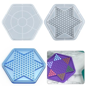 Könnte beinhalten: Zwei Silikonformen zum Herstellen eines sternförmigen Spielbretts. Eine Form ist ein klares Sechseck mit einem sternförmigen Design im Inneren. Die andere Form ist ein klares Sechseck mit einem kreisförmigen Design im Inneren. Die Formen werden neben einem fertigen Spielbrett mit bunten Murmeln gezeigt.