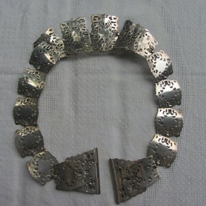 May include: A silver necklace featuring a delicate, intricate design. The necklace is made up of multiple small, connected pieces that form a circular shape.