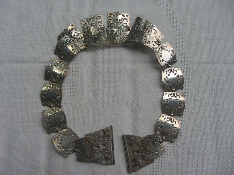 May include: A silver necklace featuring a delicate, intricate design. The necklace is made up of multiple small, connected pieces that form a circular shape.