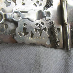 May include: Silver-toned metal clasp with intricate cut-out design and spring closures. The clasp is marked "Imprint's".